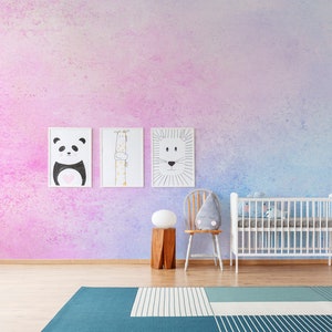 Puede incluir: Una cuna blanca con un colchón blanco y una manta con estampado gris y blanco. Hay una silla blanca con una almohada gris y un taburete de madera con una lámpara blanca encima. La pared está pintada en un degradado de rosa y azul con tres ilustraciones de animales enmarcadas.