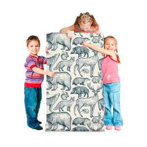 May include: Two children stand on either side of a roll of wallpaper featuring a repeating pattern of blue and white illustrations of forest animals, including bears, deer, foxes, and rabbits.