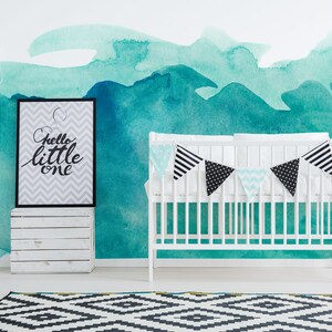 Puede incluir: Una cuna blanca con una guirnalda negra y blanca colgada encima. La cuna está delante de una pared con un diseño de acuarela turquesa. Una impresión enmarcada con el texto "hello little one" está en una caja de madera blanca.