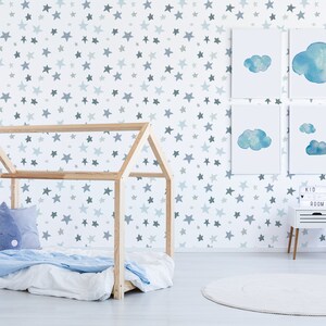 May include: A white wall with a blue and gray star pattern wallpaper. There is a wooden house-shaped bed frame with a blue and white blanket and a blue pillow with a cloud design. There are four framed watercolor paintings of clouds on the wall. A white nightstand with a sign that says "Kid Room" is next to the bed. There is a white round rug on the floor.