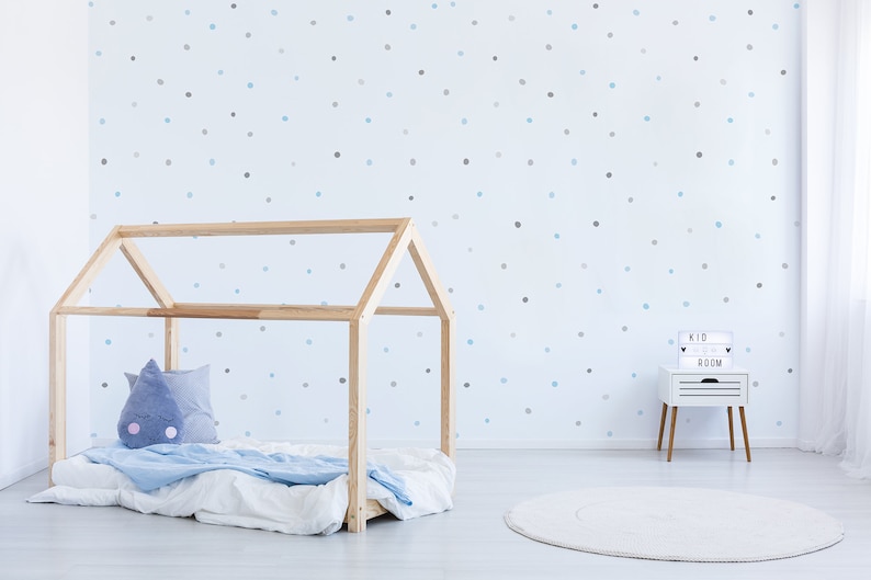 May include: A light blue and gray polka dot wallpaper with a wooden house-shaped bed frame and a white rug. A small white nightstand with a light box that reads "Kid Room" is in the corner.