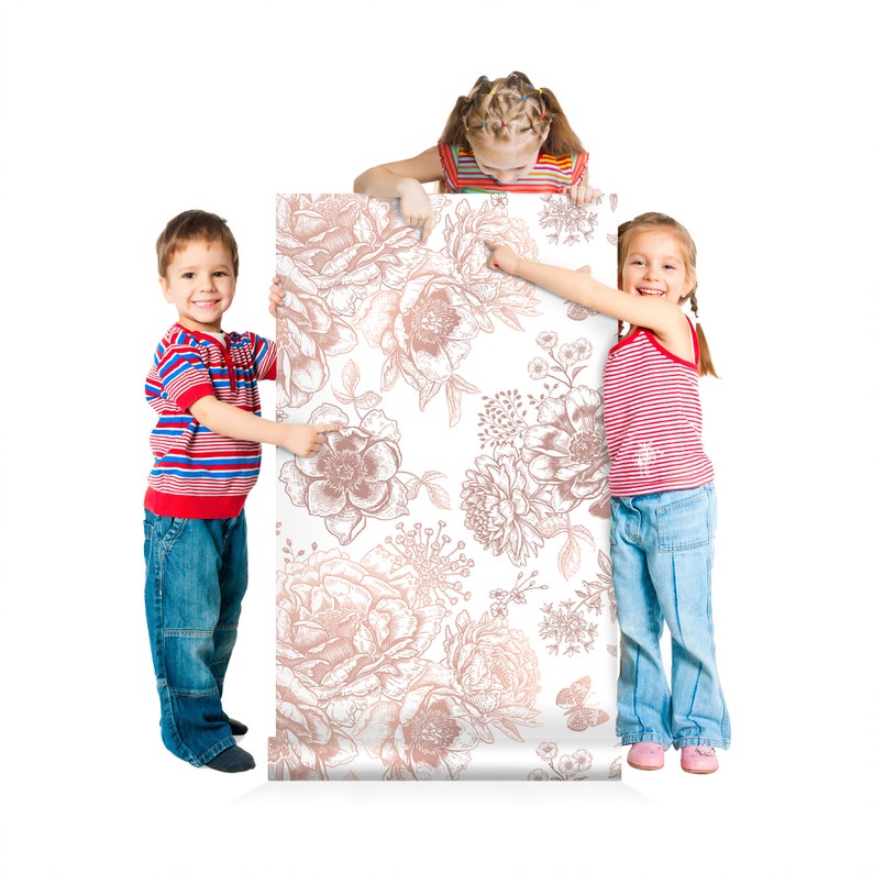 May include: Three children hold up a white and rose gold floral wallpaper roll. The wallpaper features a repeating pattern of delicate flowers and leaves.
