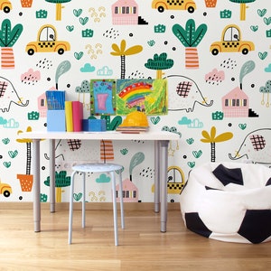 Pu&ograve; includere: Un muro bianco con una carta da parati colorata con elefanti, case, palme, auto e nuvole. Una scrivania bianca con uno sgabello bianco e un pouf bianco con un motivo a pallone da calcio nero sono di fronte al muro.
