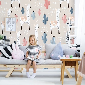 Puede incluir: Una habitaci&oacute;n infantil con papel pintado beige con motivos de llamas y cactus. Un letrero enmarcado dice "DON'T GROW UP IT'S A TRAP". Una ni&ntilde;a est&aacute; sentada en un sof&aacute; gris con cojines, leyendo. Tambi&eacute;n se ve una mesita auxiliar y un escritorio de madera.