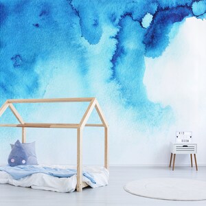 Puede incluir: Un mural de pared de acuarela azul claro con un marco de cama de madera y una mesita de noche blanca con un letrero que dice "Kid Room".