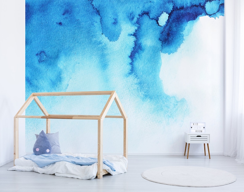 Puede incluir: Un mural de pared de acuarela azul claro con un marco de cama de madera y una mesita de noche blanca con un letrero que dice "Kid Room".