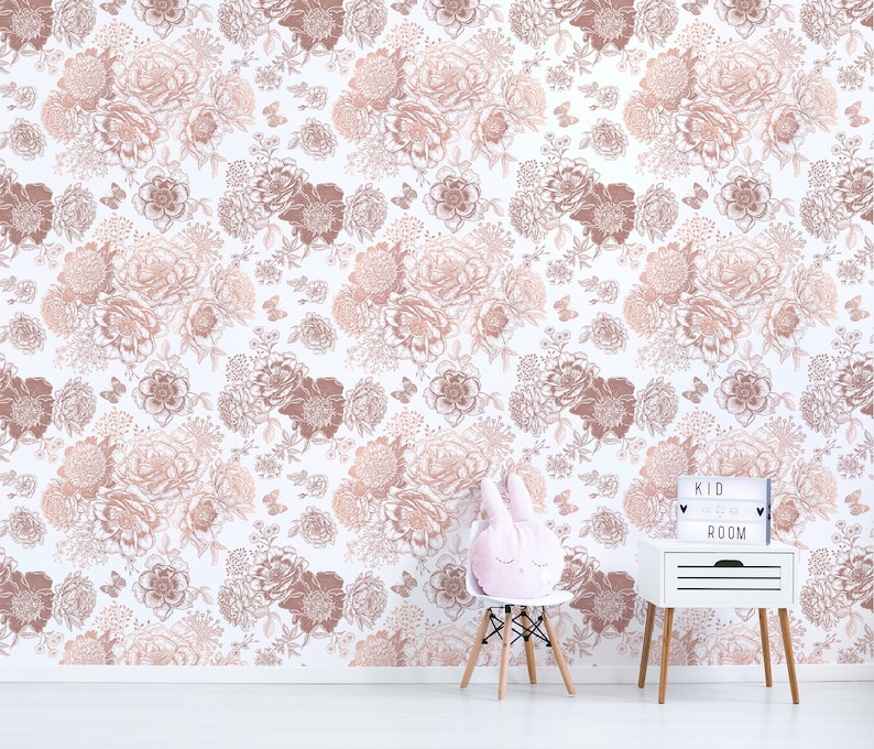 May include: A white wall with a floral wallpaper pattern in shades of pink and brown. The wallpaper features a repeating pattern of flowers and butterflies. A white bedside table with a wooden top and a white light box with the text "KID ROOM" is in the lower right corner of the image. A white chair with a pink bunny rabbit cushion is in the lower left corner of the image.
