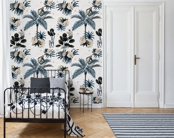 Könnte beinhalten: Eine weiße Wand mit einer blauen und weißen tropischen Tapete mit Palmen, Blumen und Affen. Vor der Wand steht ein schwarzes Metallbettgestell mit einer weiß-schwarz gestreiften Decke.
