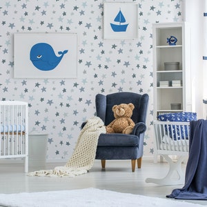 May include: A white crib with a blue and white patterned sheet, a white rocking bassinet with a blue and white patterned sheet, a blue armchair with a teddy bear sitting on it, and a white bookshelf with blue and white decorations. The room has a white wall with a blue star pattern.