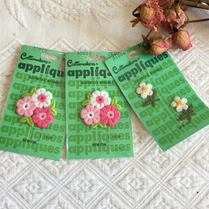 Vintage 1975 costurado em apliques de Costumakers. Duas flores brancas com centro amarelo, flores triplas rosa e brancas e folhas verdes.