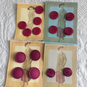 May include: Four cards with vintage illustrations of women in framed portraits, each accompanied by several magenta buttons. The buttons are round with four holes. The cards have a light blue and yellow background.