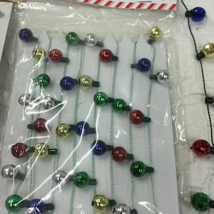 May include: A package of mini Christmas tree trimmings. The trimmings are small, round ornaments in various colors, including red, green, silver, gold, and blue. The package has the words "MINI TREE TRIMMINGS" printed on it.