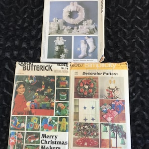 Può includere: Tre confezioni di modelli natalizi vintage. La confezione superiore presenta una ghirlanda e altre decorazioni natalizie. La confezione in basso a sinistra è etichettata "Merry Christmas Makers". La confezione in basso a destra è etichettata "Decorator Pattern".