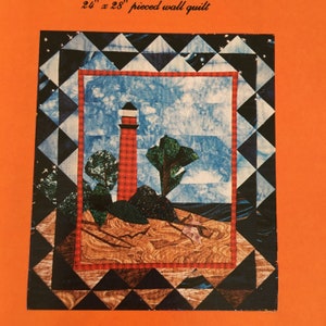 Könnte beinhalten: Ein 24 x 28 Zoll großes, zusammengesetztes Wandquilt mit einem Leuchtturm, Bäumen und einer Sandstrand-Szene. Das Quilt ist mit einem schwarzen und weißen Diamantenmuster gerahmt.