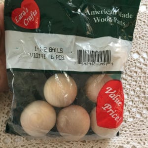 May include: A clear plastic bag containing six unfinished wooden balls. The bag has a label that reads "Lara's Crafts" and "American Made Wood Parts." The label also indicates the balls are 1-1/2 inches in diameter. A red sticker says "Value Price!"