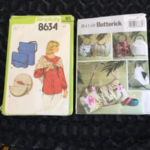 May include: Two vintage sewing pattern envelopes. The Simplicity pattern 8634 features illustrations of a woman and bags. The Butterick pattern B4148 shows various purse designs with floral and striped patterns. Both are on a black lace surface.