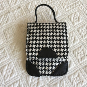 Puede incluir: Un pequeño bolso de mano de color blanco y negro con estampado de pata de gallo, con asa y ribetes de cuero negro.