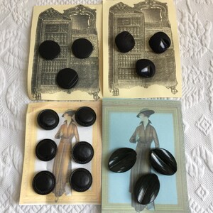 May include: A collection of black buttons in various shapes and sizes, arranged on vintage-style cards. The buttons include round and oval designs, some with textured surfaces. The cards feature illustrations of antique furniture and women in period clothing.
