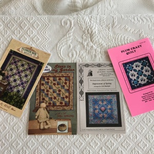 Può includere: Quattro libri di modelli di quilting con disegni colorati. I titoli sono "Flower Box Quilts", "Stars in my Garden", "Granny Nanny's Quilting Gadgets: Impressions of Spring" e "Plum Crazy Quilt".