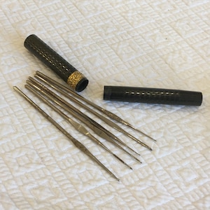 May include: A set of eight silver knitting needles in a black and gold case. The needles are arranged in a fan shape and the case is open.