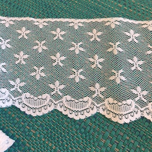 May include: Off-white lace trim featuring a floral pattern. The lace has a scalloped edge and a delicate, open weave design. This trim is suitable for various craft and sewing projects.