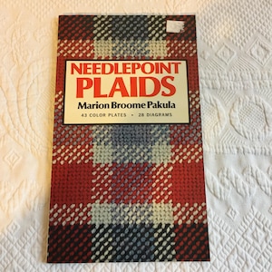 May include: A vintage book titled "Needlepoint Plaids" by Marion Broome Pakula. The cover features a plaid pattern in red, white, blue, and black. The book includes 43 color plates and 28 diagrams, perfect for needlepoint enthusiasts.