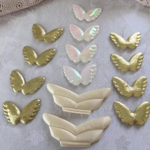 May include: A collection of decorative butterfly wings in various styles. Some are gold, textured fabric, others are iridescent, and some are a creamy white. These embellishments are ideal for crafts and DIY projects.