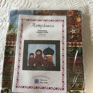 May include: A quilting pattern for a 19 1/2 by 16 1/2 inch project called "Матрёшка" (Matryoshka) Russian Dolls. The pattern features a colorful illustration of five nesting dolls and a church with a dome.