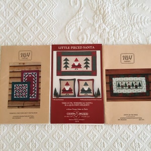 Peut inclure: Trois patrons de quilting sur papier pour fondation représentant le Père Noël et des sapins. Les patrons sont intitulés "Little Pieced Santa", "Pinwheel Pines Quilt and Runner", et "Santa in the Pines".