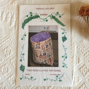 Può includere: Un modello di cucito per un raccoglitore di fili, intitolato "TWO PEAS in a POD" patterns. Il modello è illustrato con un raccoglitore di fili in tessuto colorato con una fodera viola.