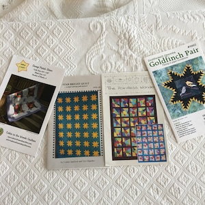 May include: Four quilting patterns with titles "Serap Patch Stars", "Star Bright Quilt", "The Pointless Wonder", and "Goldfinch Pair". The patterns are printed on white paper with colourful illustrations.