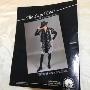 May include: A black and white patterned lapel coat with a black collar and a black belt. The model is wearing a black hat and the text "Wear it open or closed!" is printed below the image. The text "Judy Bishop Designs 1995" is printed in the bottom left corner.