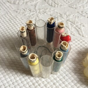 May include: A clear plastic container with 10 spools of thread. The spools are in various colors, including red, blue, green, yellow, and brown. The spools are labeled with the word "Ober" and the word "Yarn".