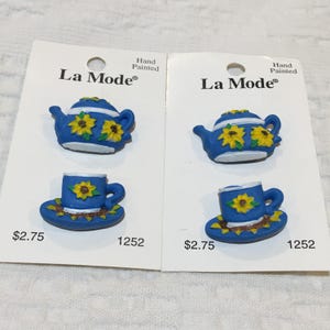 Puede incluir: Dos tarjetas que muestran un juego de tetera y taza azules con detalles de girasoles. Las tazas están sobre platillos. Las tarjetas están etiquetadas como "La Mode" y "Pintado a mano".