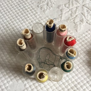 May include: A clear plastic thread organizer with 10 spools of thread in various colors, including red, blue, pink, yellow, and brown. The spools are labeled with the word "BERN".