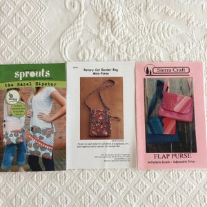 May include: Three sewing patterns for bags. The first pattern is for a Hazel Hipster bag with two style options. The second pattern is for a rotary cut border bag mini-purse. The third pattern is for a flap purse with four pockets inside and an adjustable strap.
