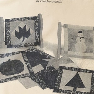 May include: Black and white quilted squares with different seasonal designs. The designs include a maple leaf, a snowman, a pumpkin, a square, and a Christmas tree.