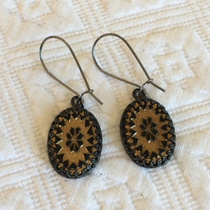 May include: A pair of gold and black oval earrings with a geometric design. The earrings have a simple wire hook closure.
