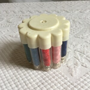 May include: A white plastic spool holder with a flower-shaped top. The holder contains eight spools of thread in various colors, including blue, red, pink, and white.