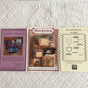 May include: Three sewing patterns for quilting projects. The first pattern is titled "A Quilter's Necessary" and shows a quilted pouch with multiple pockets. The second pattern is titled "Four Corners: Aunt Sally's Sewing Machine Cover" and shows a sewing machine cover with a patchwork design. The third pattern is titled "Decorative Window Pockets" and shows a variety of pocket designs.