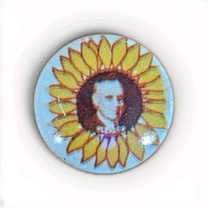 May include: A round button featuring a portrait within a sunflower design. The sunflower has yellow petals and a brown center. The portrait is of a person with light skin and dark hair, set against a light blue background.
