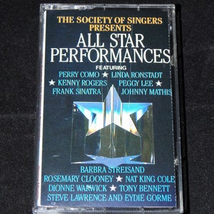 Puede incluir: Una cinta de casete con un diseño de estrella azul y blanca con el texto "The Society of Singers Presents All Star Performances" y una lista de artistas que incluye a Perry Como, Linda Ronstadt, Kenny Rogers, Frank Sinatra, Peggy Lee, Johnny Mathis, Barbra Streisand, Rosemary Clooney, Nat King Cole, Dionne Warwick, Tony Bennett, Steve Lawrence y Eydie Gorme.