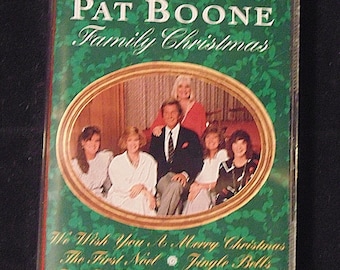 Op de afbeelding: Een groene cassetteband met een gouden rand en een foto van Pat Boone en zijn familie. De tekst op de cassetteband luidt "The Pat Boone Family Christmas" en "We Wish You A Merry Christmas, The First Noel, Jingle Bells, Joy To The World and More!" De cassetteband is gelabeld met "LaserLight".