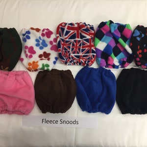 May include: A collection of fleece snoods in various colors and patterns. Designs include paw prints, a Union Jack, and geometric shapes. The snoods are displayed on a white surface, with the text "Fleece Snoods" at the bottom.