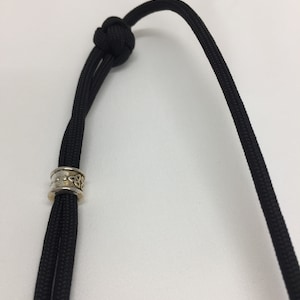 May include: A black paracord lanyard with a silver and gold Celtic knot bead.