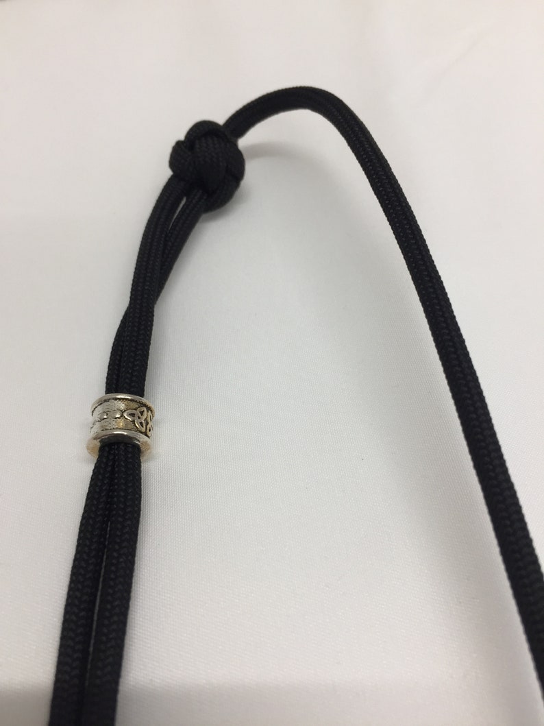 May include: A black paracord lanyard with a silver and gold Celtic knot bead.