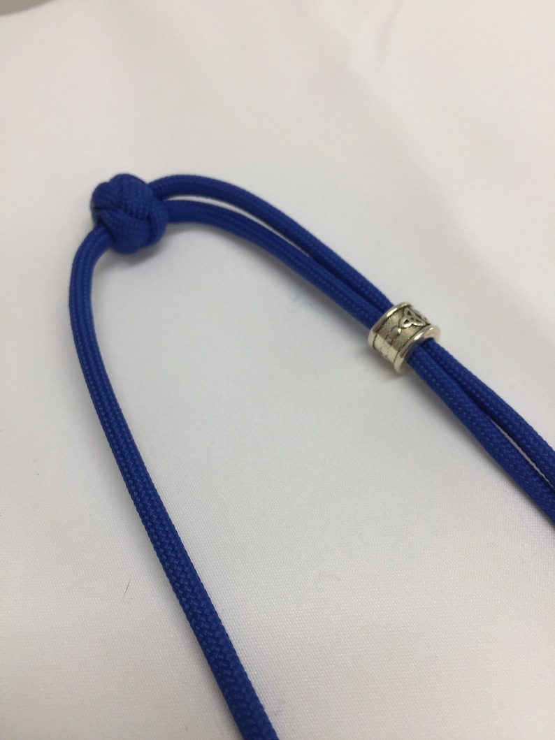 May include: A blue paracord necklace with a silver bead featuring a Celtic knot design.