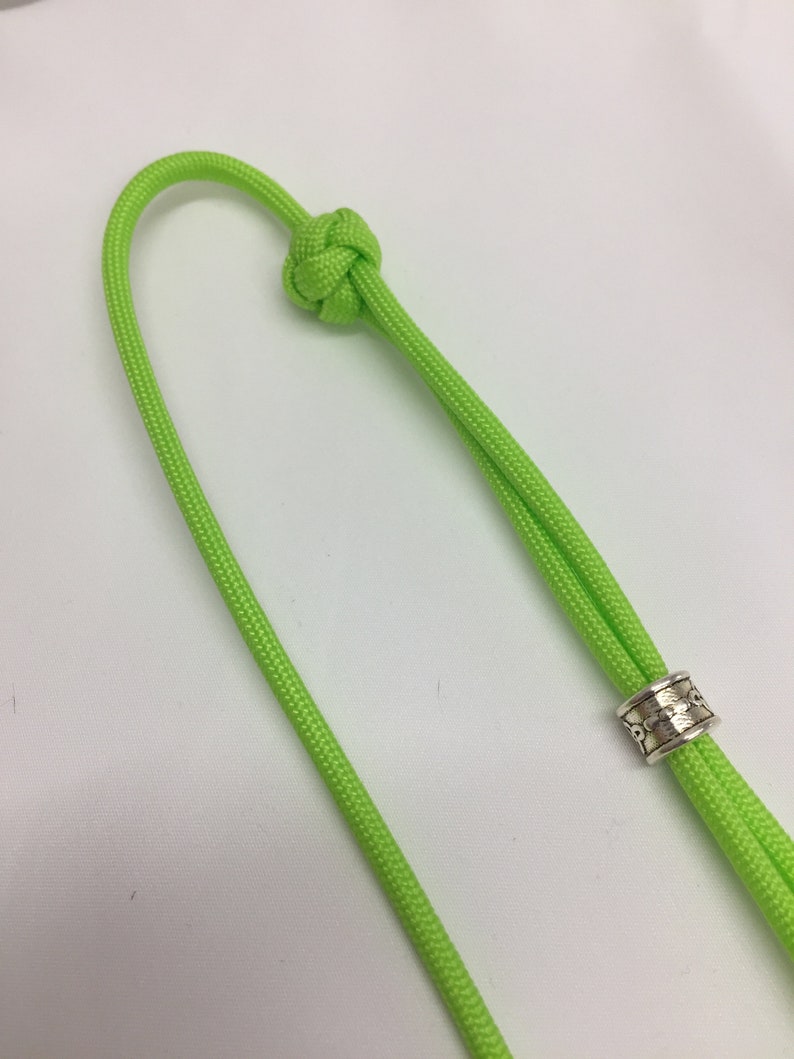 May include: A lime green paracord cord with a knot at one end and a silver bead at the other end.
