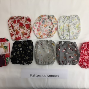 May include: A collection of patterned snoods, each with a unique design. The snoods feature various festive patterns, including Christmas themes with reindeer and snowmen, and other designs with bears, eggs, and snowflakes. The text "Patterned snoods" is visible.
