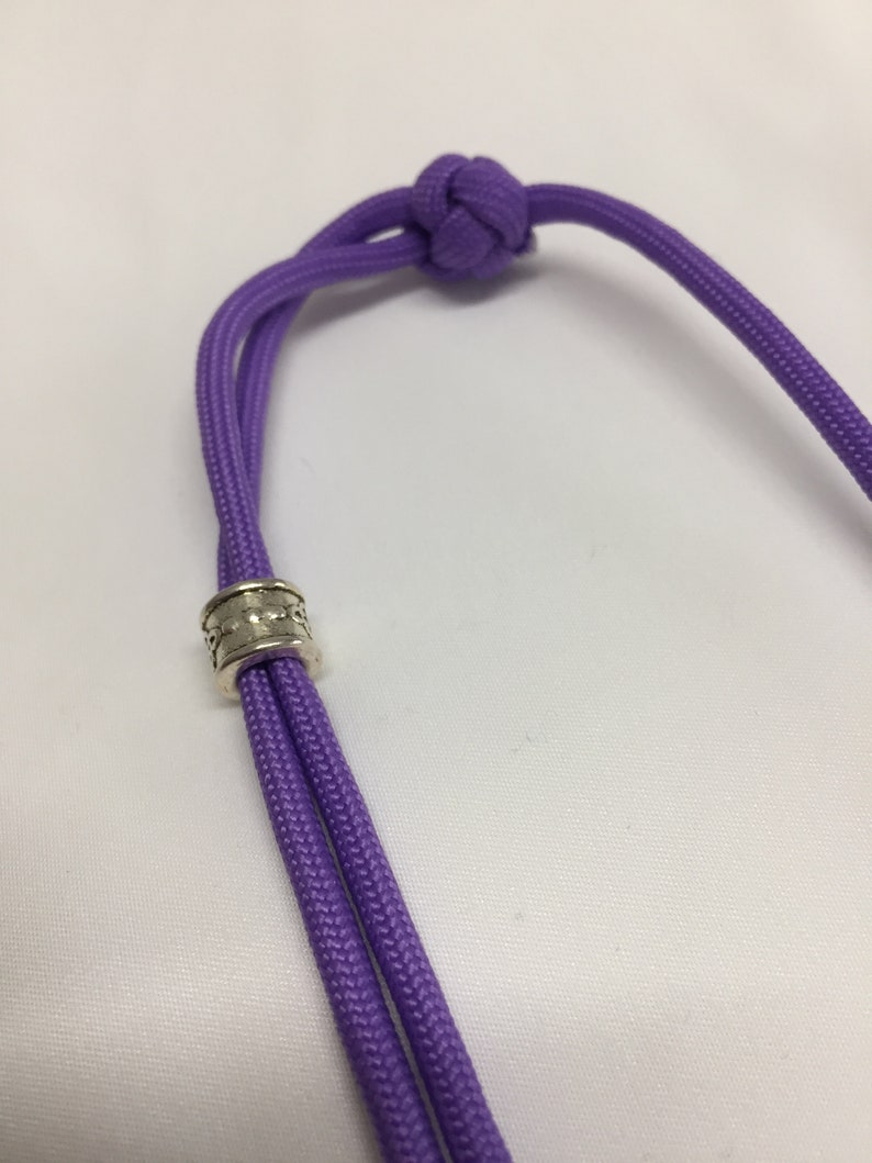 May include: A purple paracord lanyard with a silver bead. The lanyard is tied with a knot at the top.